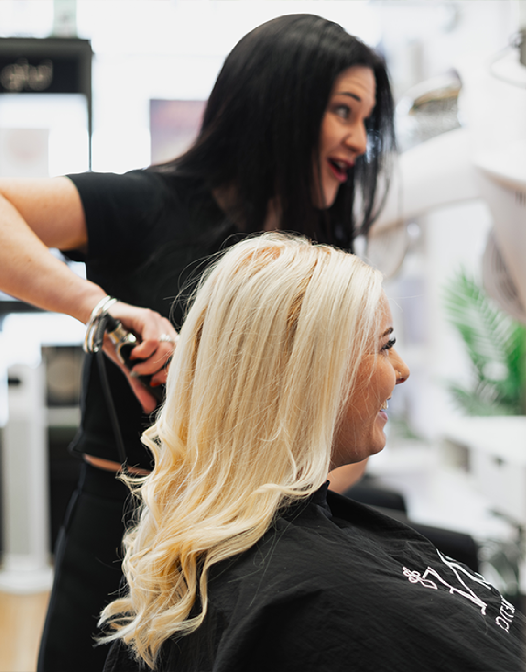 Photo of Natalie Parry, owner of Sax Hair Design, working on a client's hair in the salon. Both women are smiling.